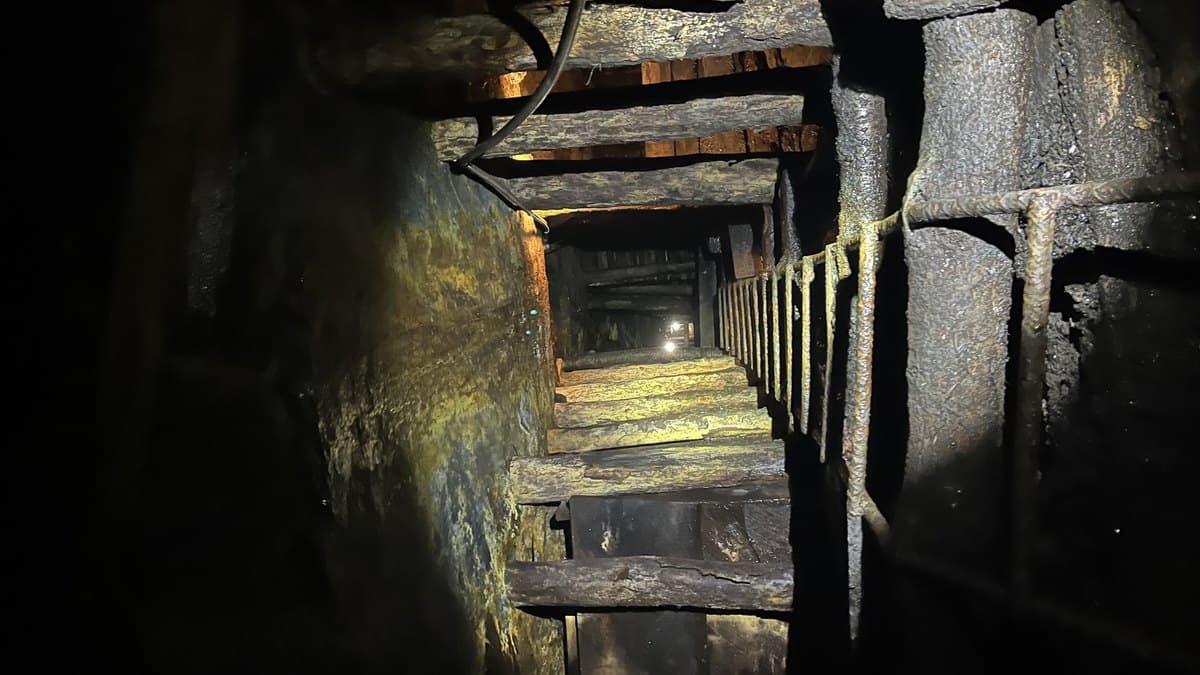 Túnel minero subterráneo con enmaderado tradicional, cableado eléctrico y luminarias de techo en galería activa