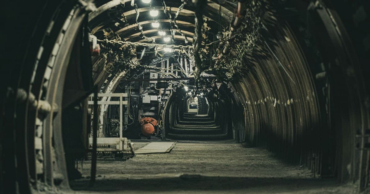 Galería de una mina subterránea con arcos de acero, cables eléctricos sujetos al techo y a las paredes, cajas eléctricas y luminarias