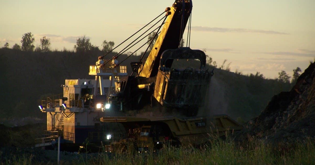 Pala eléctrica de cable cargando un camión de acarreo al atardecer en una operación minera