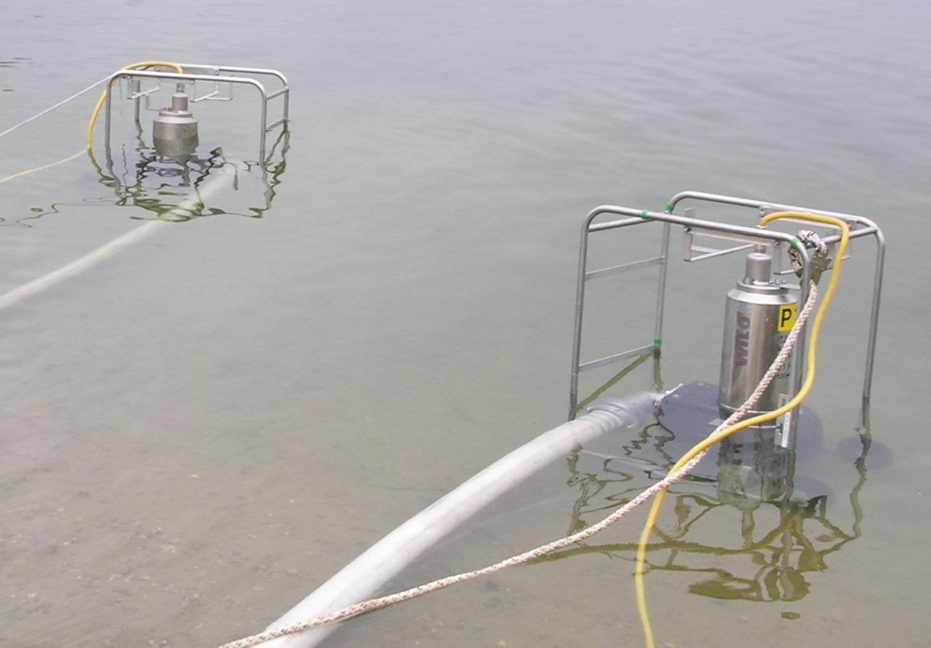 Fotografía real de dos bombas sumergibles industriales de drenaje operando en estanque de obra con cables redondos impermeables sellados en la entrada superior