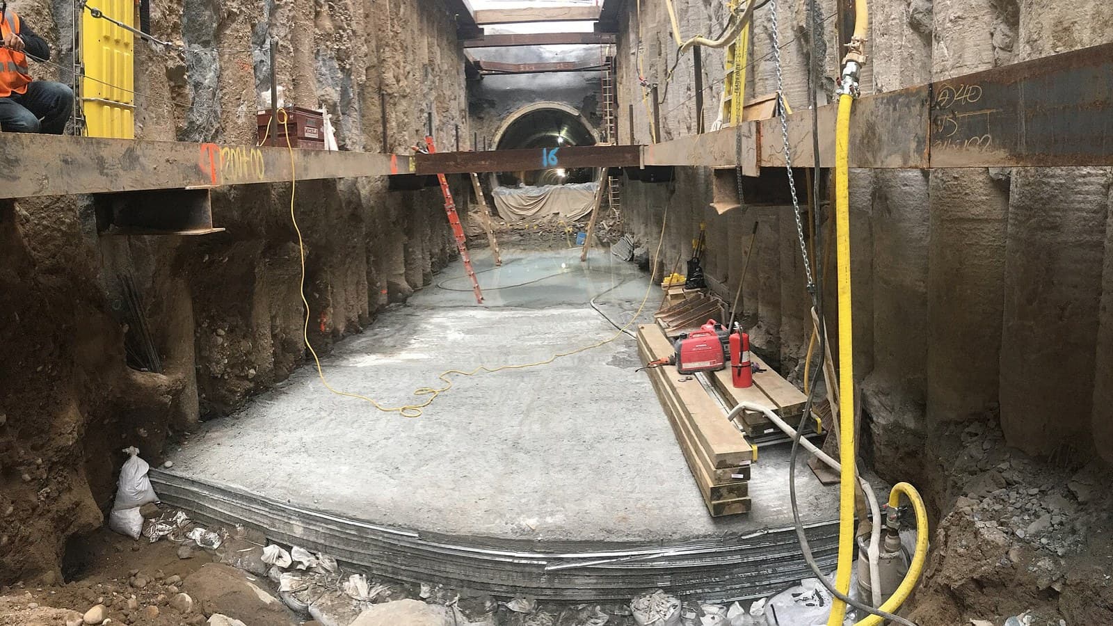 Fotografía real de obra subterránea inundada con tendido de cables eléctricos industriales de uso rudo alimentando equipos de bombeo y excavación