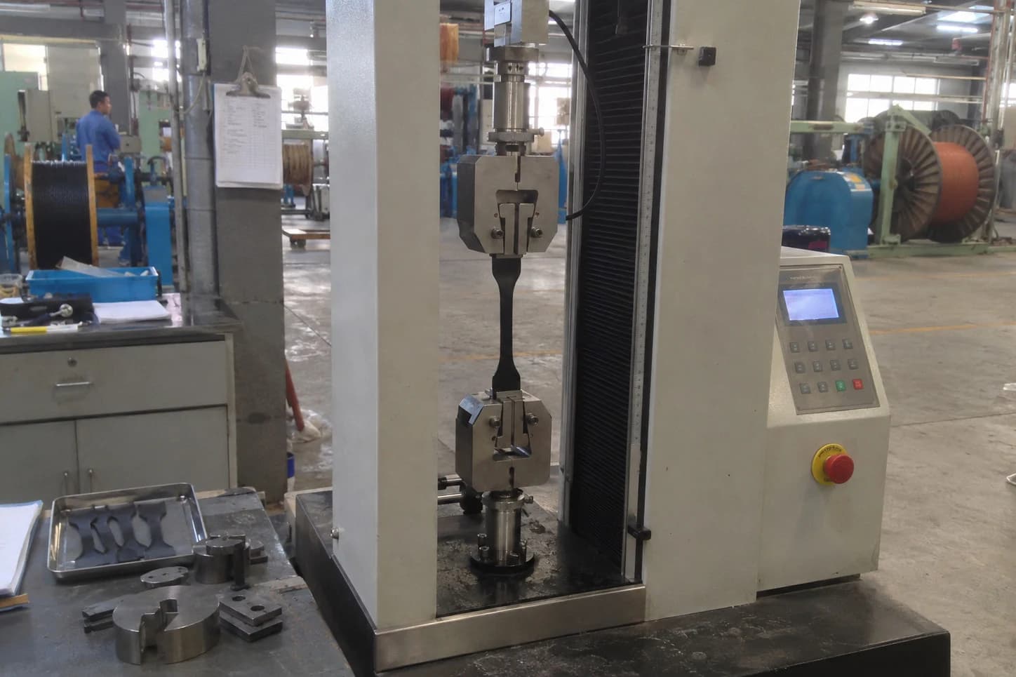 Máquina universal de ensayos realizando prueba de resistencia a la tracción y elongación hasta ruptura en probeta de cubierta minera